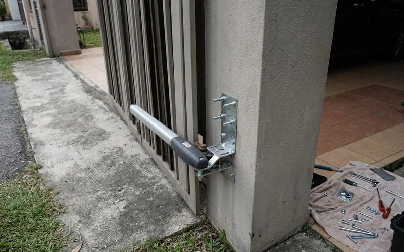 Technician conducting site assessment measuring gate pillar width and driveway clearance for swing arm installation